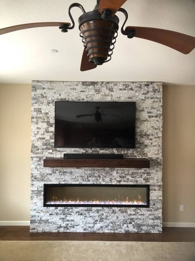 Stone fireplace wall with a solid wood mantel and a mounted television.
