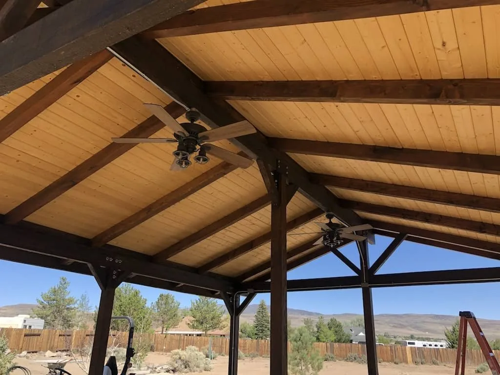 Underside of a patio cover showing stained beams, tongue and groove decking, and ceiling fans, with the Reno hills beyond.