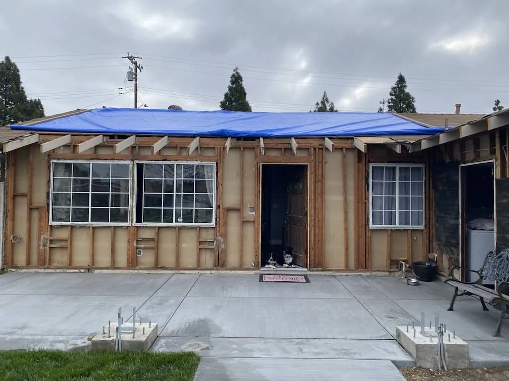 House front stripped to framing with a tarp over the roof line, mid remodel.