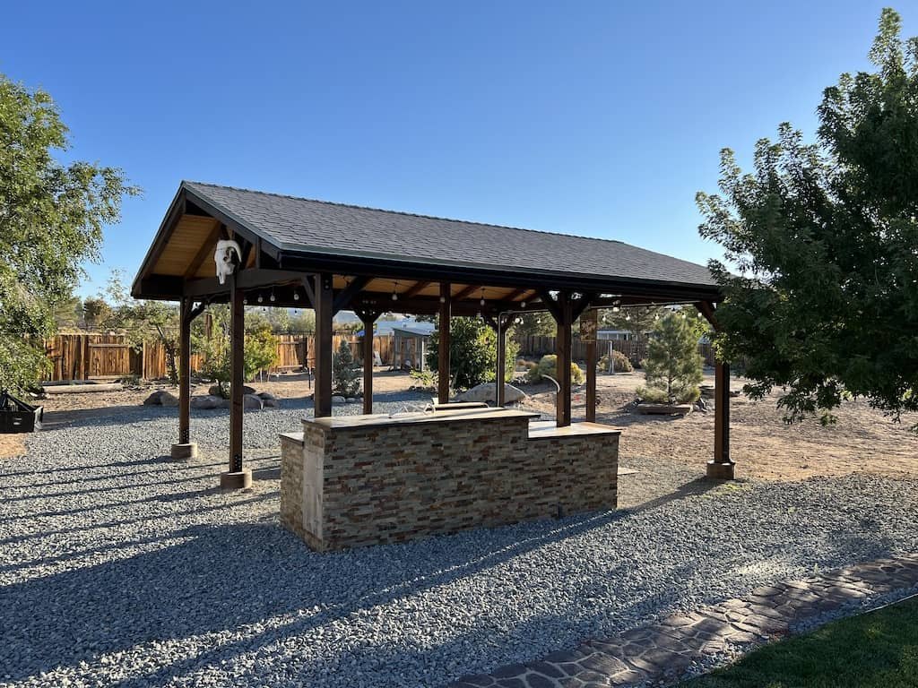 Freestanding patio cover with timber posts and a stone-faced outdoor bar in a Reno backyard.