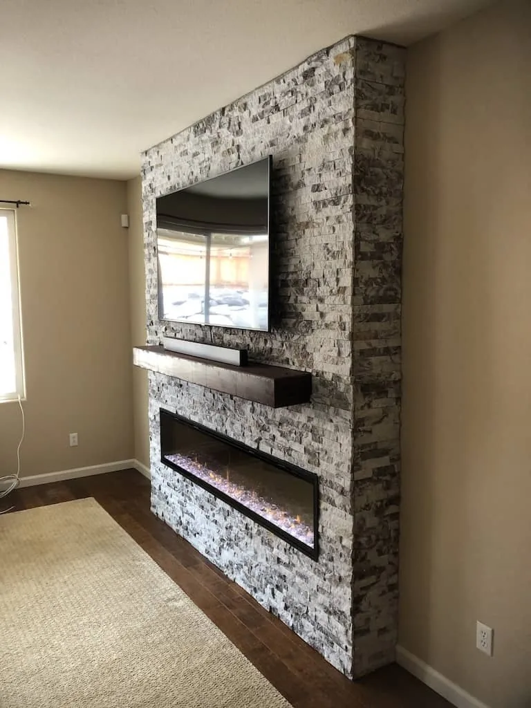 Stacked stone fireplace wall with a wood mantel and a linear fireplace.